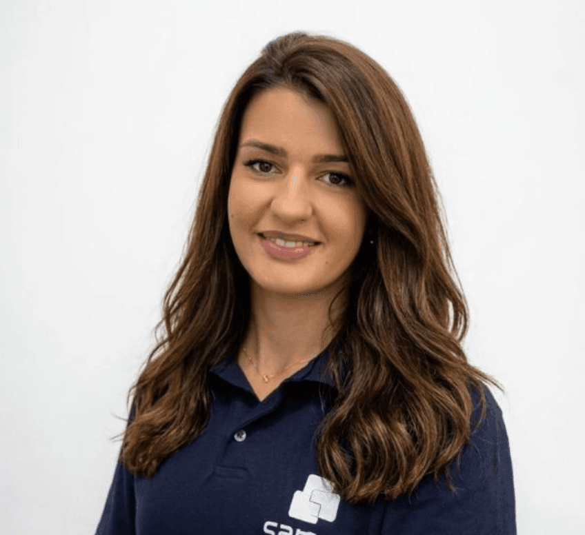 Mulher sorridente com cabelos castanhos longos e ondulados, vestindo uma camisa polo azul marinho.