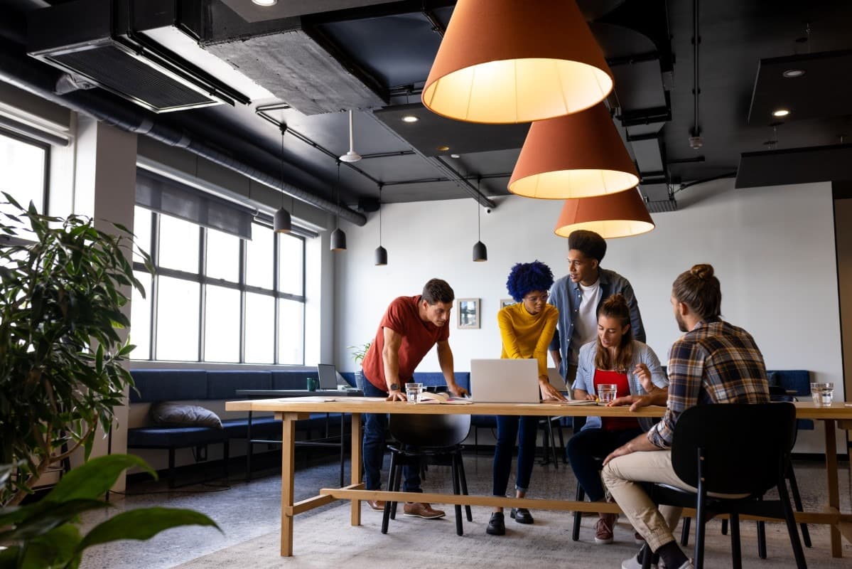 Equipe diversa trabalhando em um laptop sobre mesa de madeira em escritório moderno e iluminado.